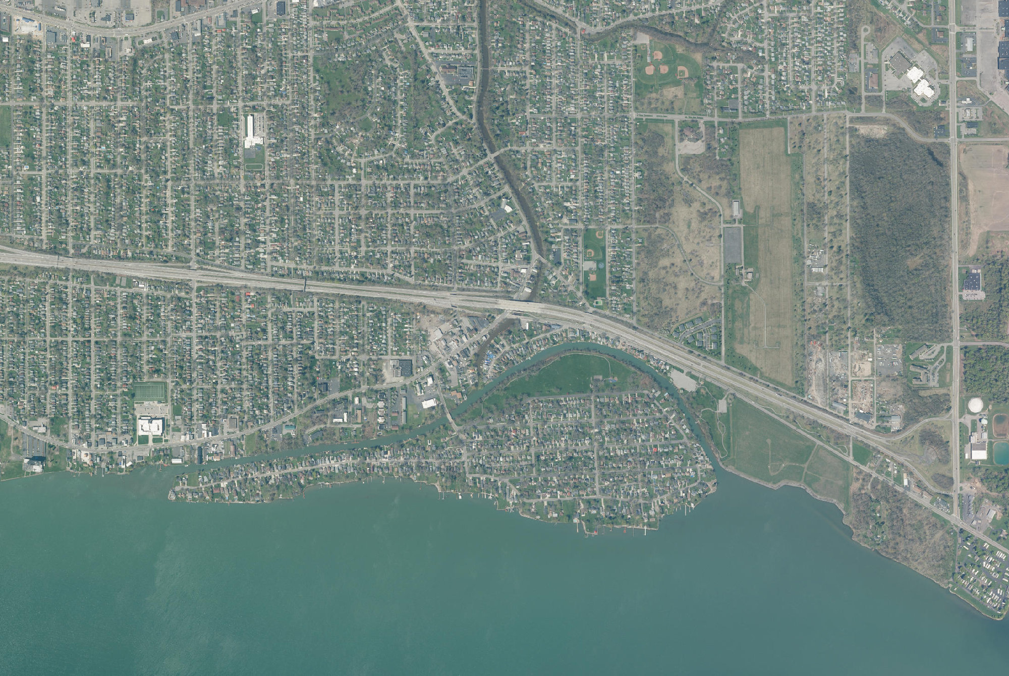 Aerial photograph showing Cayuga Island in the lower half of the frame and the cleared, capped Love Canal containment site in the upper right, less than half a mile from the island’s eastern end.